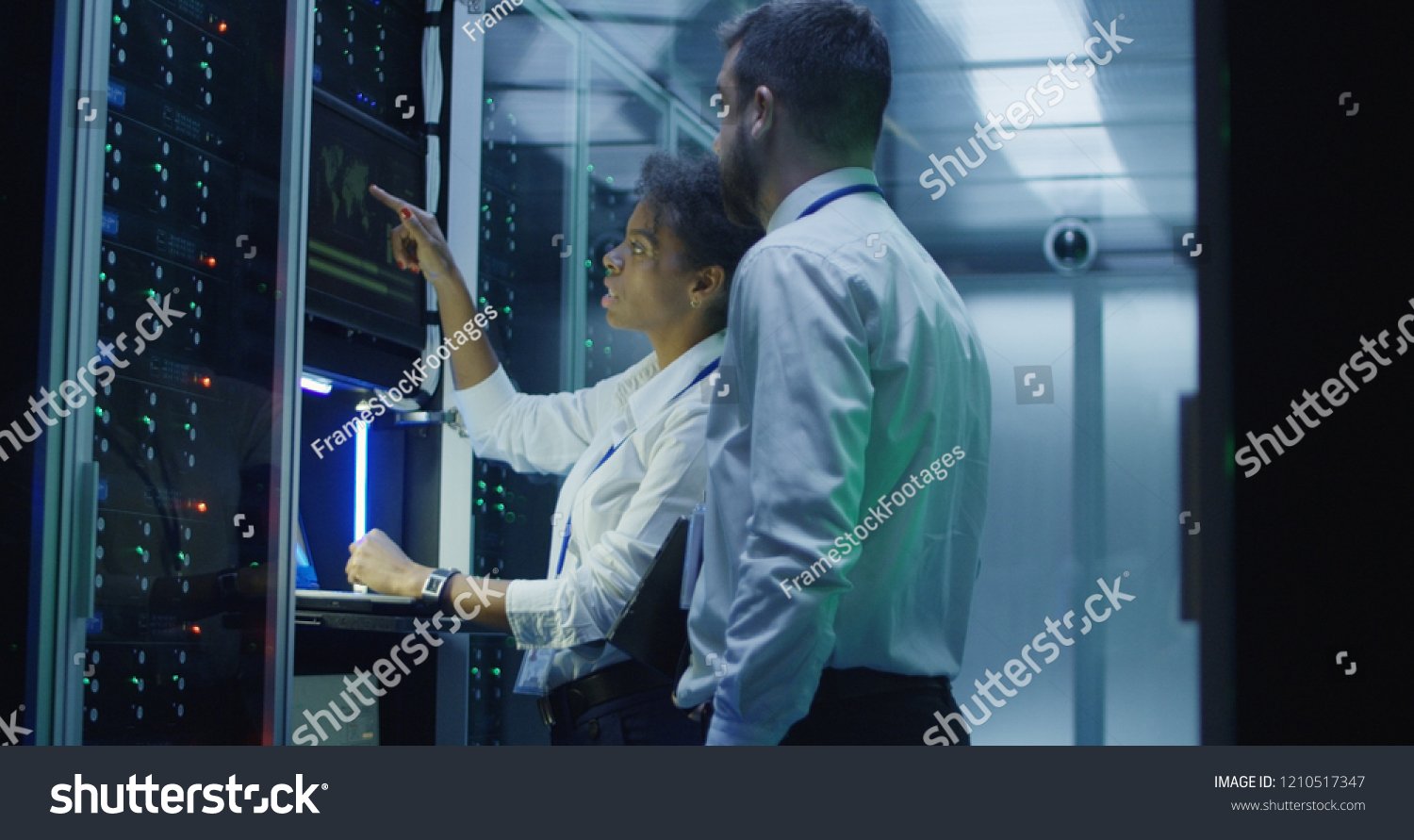 stock-photo-multiethnic-man-and-woman-in-white-shirts-using-laptop-and-tablet-while-working-in-server-room-of-1210517347